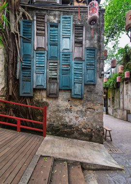 Kwai Chai Hong, Kuala Lumpur, Malezya. Mavi panjurlu yıpranmış bir bina, büyük ağaç kökleri, kırmızı korkuluklar, ve tarihi bir sokakta geleneksel Çin fenerleri.