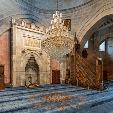 Kayseri Büyük Camii 'nin çarpıcı iç mimarisi, Türkçe: Ulu Camii, Kayseri, Türkiye. Süslü mihrab, karışık oyulmuş minbar, ve üzerinde büyük kristal avize desenli mavi halı