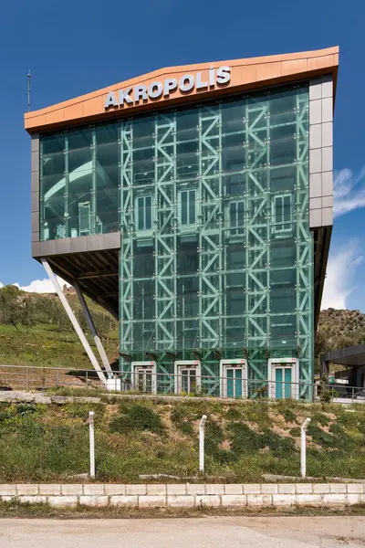 AKROPOLIS işareti taşıyan Pergamon Acropolis Kablo Otomobil İstasyonunun modern cam binası, Bergama, İzmir, Türkiye. Güneşli gün, mavi gökyüzü, yeşil yamaç