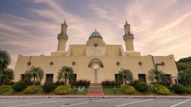 Ash Shaliheen Camii, Bandar Seri Begawan, Brunei Darussalam. Altın saatinde minareleri, kubbesi ve palmiyeleri olan kum renkli İslami mimari cephesi