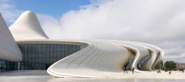 Baku, Azerbaijan - May 7, 2024: Heydar Aliyev Center. Iconic modern architecture with flowing white lines and glass facade under a cloudy sky. People on the plaza