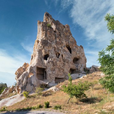 Iconic fairy chimney rock formation with ancient cave dwellings at Goreme Open-Air Museum, Cappadocia, Turkey, under a bright blue sky