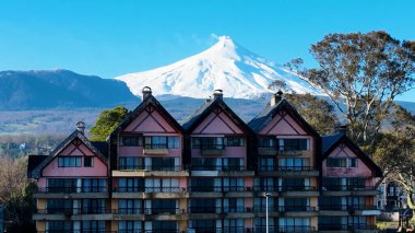 Volcano Behind Building At Pucon In Los Rios Chile. European Buildings. Vulcanic Scenery. Tourism Landscape. Pucon Chile. Volcano Background. Volcano Behind Building At Pucon In Los Rios Chile. clipart