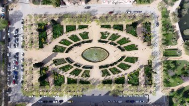 İspanya 'daki Ciutadella Parkı. İnsansız hava aracı, etrafı gür ağaçlarla çevrili kaldırımlı bir bahçe yakalıyor. Metropolitan Skyline Binaları Güzel. Bina Mimarlık Şirketi. Barselona İspanya.