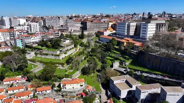 Porto Portekiz 'deki Erdemliler Parkı. İnsansız hava aracı, etrafı gür ağaçlarla çevrili kaldırımlı bir bahçe yakalıyor. Şehir merkezindeki iş dünyası. İş geçmişleri ünlüdür. Porto Portekiz.