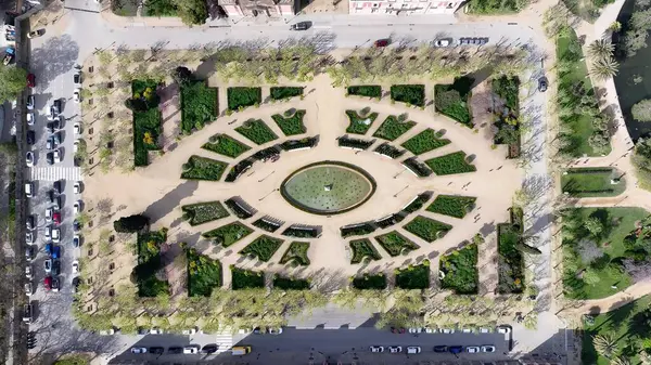 İspanya 'daki Ciutadella Parkı. İnsansız hava aracı, etrafı gür ağaçlarla çevrili kaldırımlı bir bahçe yakalıyor. Metropolitan Skyline Binaları Güzel. Bina Mimarlık Şirketi. Barselona İspanya.