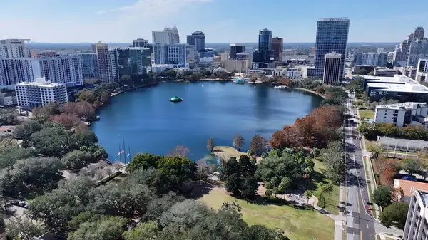 Orlando Skyline Orlando Florida Birleşik Devletleri 'nde. İnsansız hava aracı, etrafı gür ağaçlarla çevrili kaldırımlı bir bahçe yakalıyor. İş Bulutları Gökyüzü Şehir Merkezi. Panoramik Şehir. Orlando Florida.