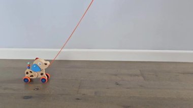 Tahta köpek minimalist sahnede tahta zeminde hareket eder. Tahta bir köpek oyuncağı çerçevenin bir tarafından diğer tarafına ahşap bir zeminde seyahat eder. Elleri ya da insanları görünmüyor. Yumuşak ışıklandırmalı ve rahat bir ev atmosferli minimalist oyuncak sahnesi.