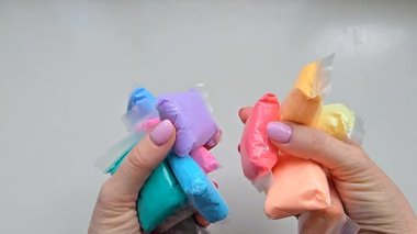 Eller masaya yumuşak pastel tonlu mankenlik kil paketleri fırlatır. Tatmin edici ve dinamik hareket, DIY ve yaratıcı aktiviteler için canlı el sanatları malzemeleri sergilenmesi.