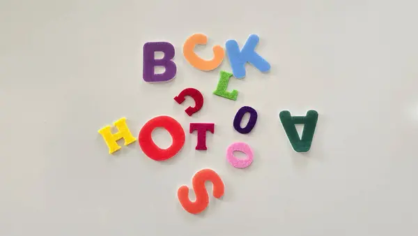 Beyaz bir masaya dağılmış renkli keçeli harflerle 