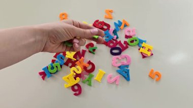 Beyaz bir masanın üzerindeki dağınık bir yığından rengarenk keçeli harfler ve numaralar seçiyor. El yapımı yumuşak alfabeyle DIY eğitim zanaatı ve öğrenme ve yaratıcı faaliyetler için rakamlar.