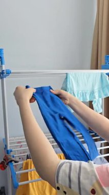 Kurutma sehpasından bebek kıyafetlerini çıkaran bir kadın. Ev hayatı, ebeveynlik ve günlük ev işleri. Doğal ışık ve sıradan atmosfer.