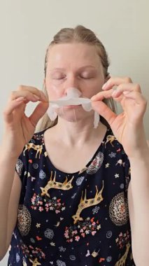 Sarışın bir kadının kumaş çarşaf maskesini çıkarırken ve nazikçe yüzüne masaj yaparken. Doğal cilt bakımı, kişisel bakım ve güzellik tedavisi. Cilt bakımı, sağlık, yüz masajı ve sabah veya akşam rutinleri gibi konular için idealdir..