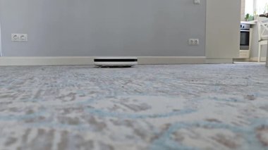 Halılı zeminde hareket eden robot elektrik süpürgesinin alçak açılı görüntüsü. Akıllı ev temizleme teknolojisi iş başında, dinamik kapalı mekan görüntüleri için zemin perspektifine yakın.