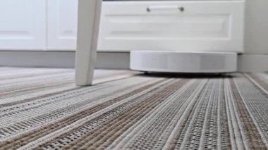 Robot elektrikli süpürge yerde hareket ediyor, sandalye bacaklarının yanından geçiyor. Akıllı ev temizliği, günlük temizlik rutinini sıcak bir iç mekanda sergilemek.