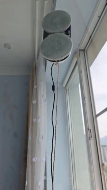 Açık bir pencerenin camını yıkayan bir cam temizleme robotunun dikey videosu, içeriden çekilmiş. Perdeler yandan görünür, doğal ışık odayı aydınlatır..