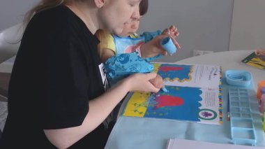 Anne ve bebek evde parmak boyalarıyla resim yapıyorlar. Yaratıcı kaynaşma zamanı, koruyucu önlüklü ve kollu çocuk. Eğlenceli dağınık oyun ve erken dönem sanat gelişimi aktivitesi.
