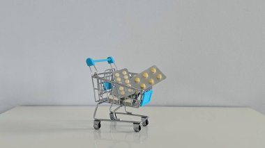 İlaç paketleriyle dolu mini alışveriş arabası modern sağlık hizmetlerini, tıbbi giderleri ve sağlık ve tüketici alışkanlıklarının kesişmesini yansıtan kavramsal bir görüntü..