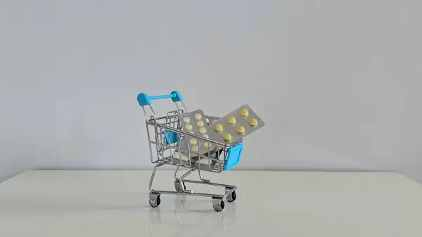 İlaç paketleriyle dolu mini alışveriş arabası modern sağlık hizmetlerini, tıbbi giderleri ve sağlık ve tüketici alışkanlıklarının kesişmesini yansıtan kavramsal bir görüntü..