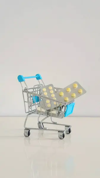 İlaç paketleriyle dolu mini alışveriş arabası modern sağlık hizmetlerini, tıbbi giderleri ve sağlık ve tüketici alışkanlıklarının kesişmesini yansıtan kavramsal bir görüntü..