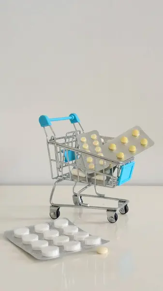İlaç paketleriyle dolu mini alışveriş arabası modern sağlık hizmetlerini, tıbbi giderleri ve sağlık ve tüketici alışkanlıklarının kesişmesini yansıtan kavramsal bir görüntü..