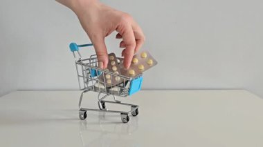 Bir el, küçük bir alışveriş arabasından gri bir arka planı, günlük sağlık hizmetlerini ve kişisel refahı temsil eden gri bir masanın üzerindeki su toplayan hapları alır..