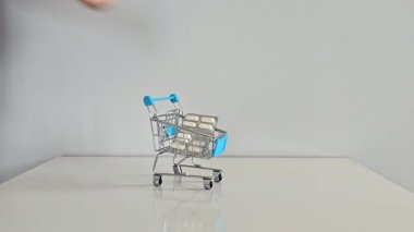 Bir el, ilaç paketlerini küçük bir alışveriş arabasına yerleştiriyor. Gri bir geçmişi olan beyaz bir masaya. Sağlık, günlük sağlık ve kişisel sağlık hizmetlerini sembolize ediyor..