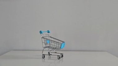 İki el dikkatle neşeli mücevherleri ve renkli Noel temalı lastik eşyaları gri arka planı olan beyaz bir alışveriş arabasının üzerine dökün..