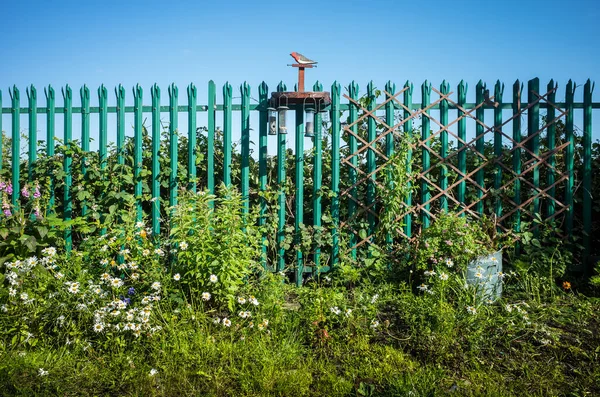 stock image A wooden bird feeder with hanging seeds and nuts along an iron urban fence.