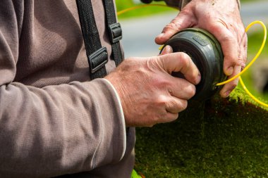 Bir adam bahçede elektrikli testereyle çimleri biçiyor. Bahçıvan çim biçme makinesiyle çim biçiyor..