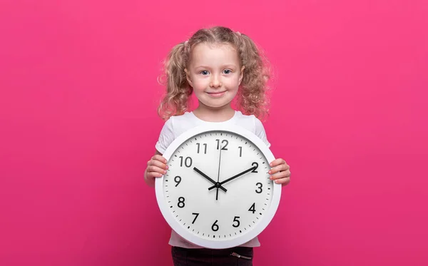 小さな女の子はピンクの背景に大きな白い時計を持っています — ストック写真