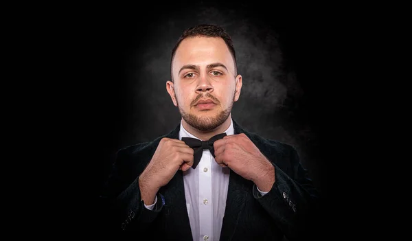 Handsome young fashionable man in a tuxedo on a dark background.