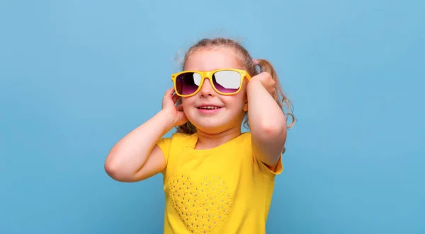 小さな女の子で黄色のサングラスで青の背景 — ストック写真