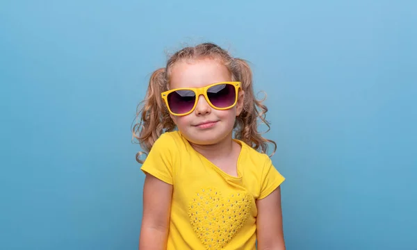 小さな女の子で黄色のサングラスで青の背景 — ストック写真