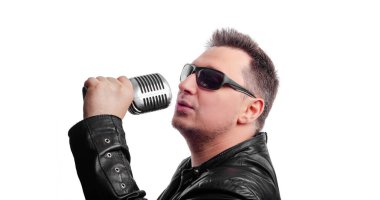 Gözlüklü bir rock şarkıcısı elinde bir mikrofonla beyaz arka planda.