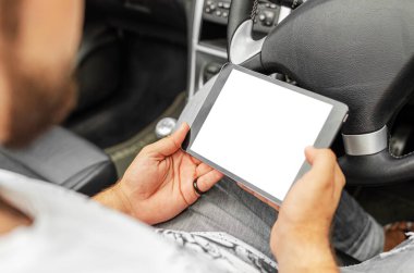 Arabasında tablet olan bir adam. Genç bir adam arabada otururken bir aletin bilgilerine bakar..