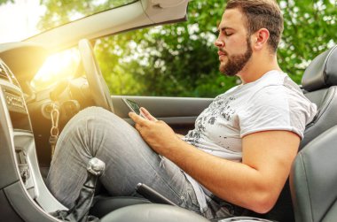 Arabasında tablet olan bir adam. Genç bir adam arabada otururken bir aletin bilgilerine bakar..
