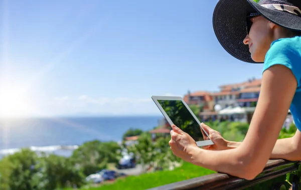 Young woman with a tablet in hands on a terrace on the background of the sea on a warm day.