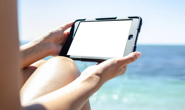 Young woman with a tablet in hands on the background of the sea on a warm day.