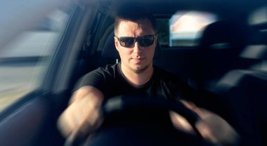 Adam bir araba kullanıyor. Siyah tişörtlü yakışıklı bir adam hızla araba sürüyor..