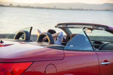 Woman in red car with open roof at background of sea water. Travel, freedom and holidays concept.
