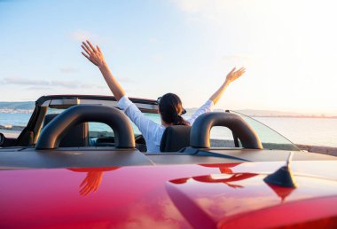 Woman in red car with open roof at background of sea water. Travel, freedom and holidays concept.
