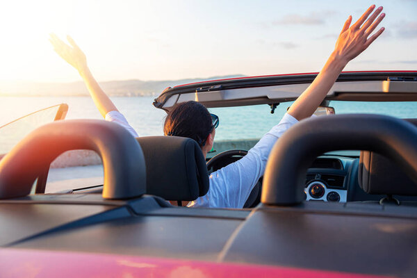 Woman in red car with open roof at background of sea water. Travel, freedom and holidays concept.