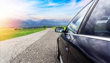 Dağların ve günbatımının arkaplanına karşı bir kır yolunda araba.