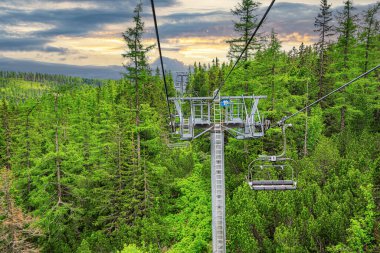 Dağlarda yükselmek. Dağın yamacındaki ormanın üstünde iki turist asansörü var..