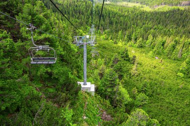 Dağlarda yükselmek. Dağın yamacındaki ormanın üstünde iki turist asansörü var..