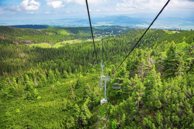 Dağlarda yükselmek. Dağın yamacındaki ormanın üstünde iki turist asansörü var..