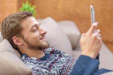 Tablet bilgisayar evde kanepede ellerinde ile pozitif delikanlı.