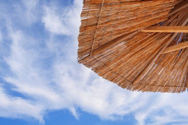 Sahilde güneşli yataklı saman şemsiyeler. Gün batımında ya da gündoğumunda kumsalda saman şemsiyeler ve güverte sandalyeleri.