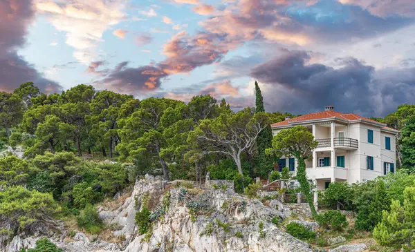 Çelişkili bir gökyüzüne karşı ormanı olan bir uçurumda ev.